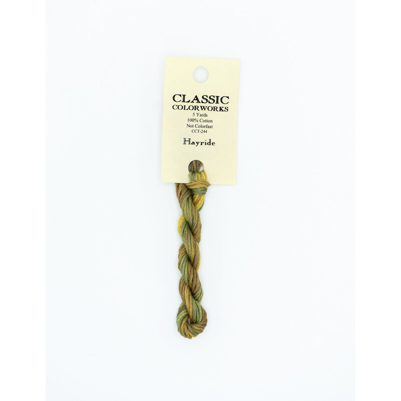 A skein of variegated sage green, yellow, and warm brown embroidery floss, twisted and bundled, with a cream and black label featuring the brand name and color information.
