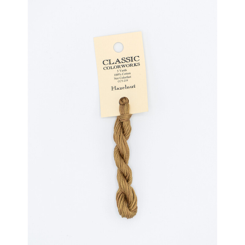 A skein of light brown embroidery floss, twisted and bundled, with a cream and black label featuring the brand name and color information.