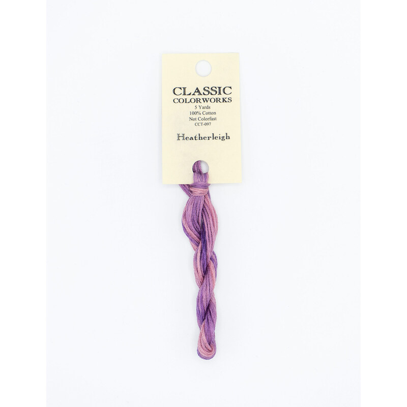 A skein of variegated pink and purple embroidery floss, twisted and bundled, with a cream and black label featuring the brand name and color information.