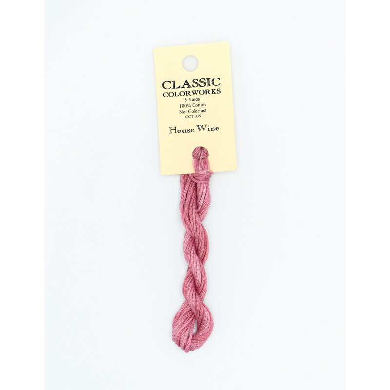 A skein of pink embroidery floss, twisted and bundled, with a cream and black label featuring the brand name and color information.