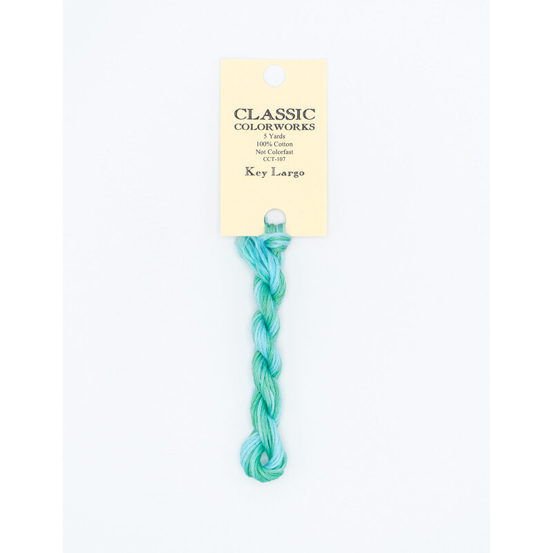 A skein of variegated mint green and aqua blue embroidery floss, twisted and bundled, with a cream and black label featuring the brand name and color information.