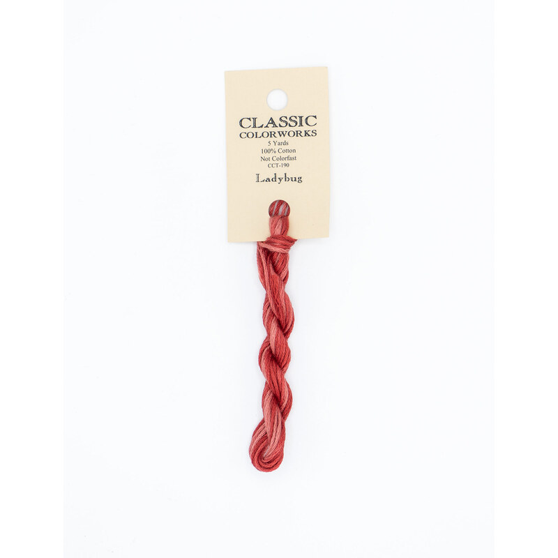 A skein of variegated red and pink embroidery floss, twisted and bundled, with a cream and black label featuring the brand name and color information.
