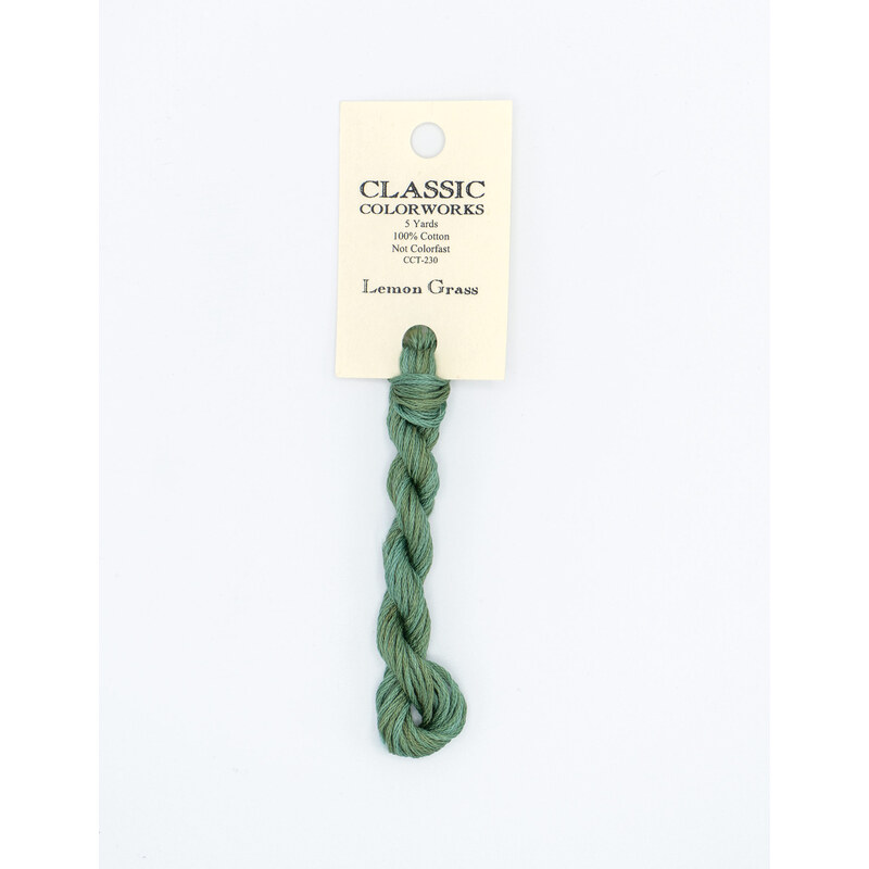 A skein of muted green embroidery floss, twisted and bundled, with a cream and black label featuring the brand name and color information.