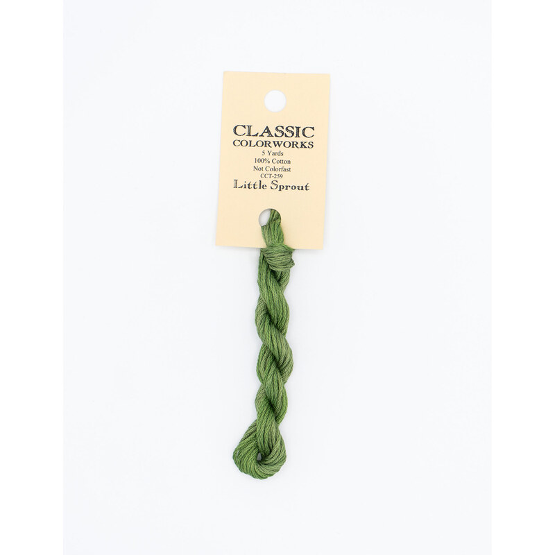 A skein of green embroidery floss, twisted and bundled, with a cream and black label featuring the brand name and color information.