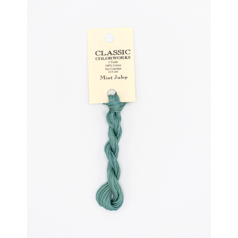 A skein of teal embroidery floss, twisted and bundled, with a cream and black label featuring the brand name and color information.