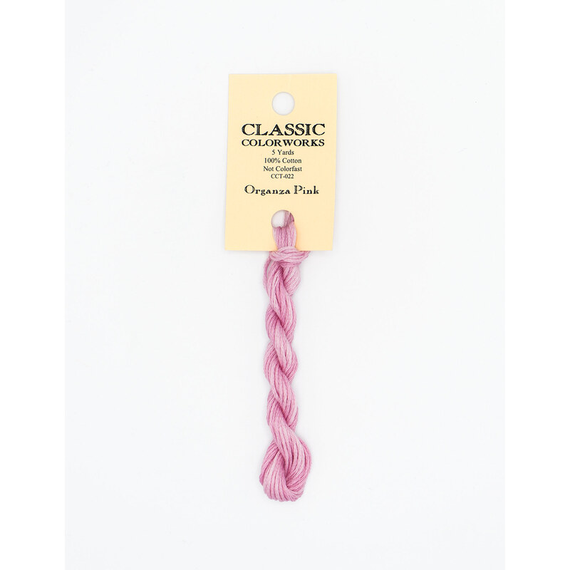 A skein of pink embroidery floss, twisted and bundled, with a cream and black label featuring the brand name and color information.