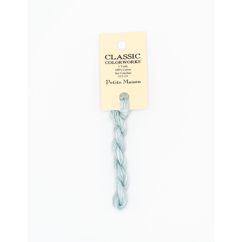 A skein of light blue embroidery floss, twisted and bundled, with a cream and black label featuring the brand name and color information.