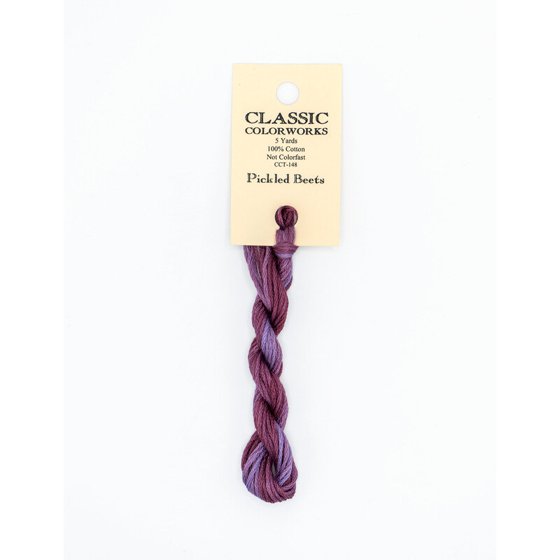 A skein of variegated purple embroidery floss, twisted and bundled, with a cream and black label featuring the brand name and color information.