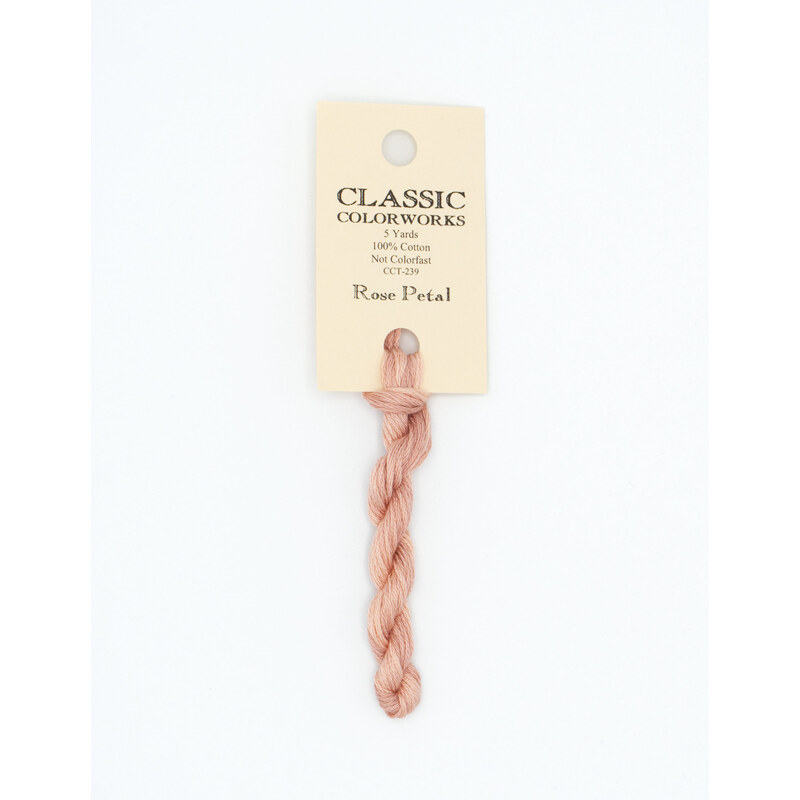A skein of coral pink embroidery floss, twisted and bundled, with a cream and black label featuring the brand name and color information.