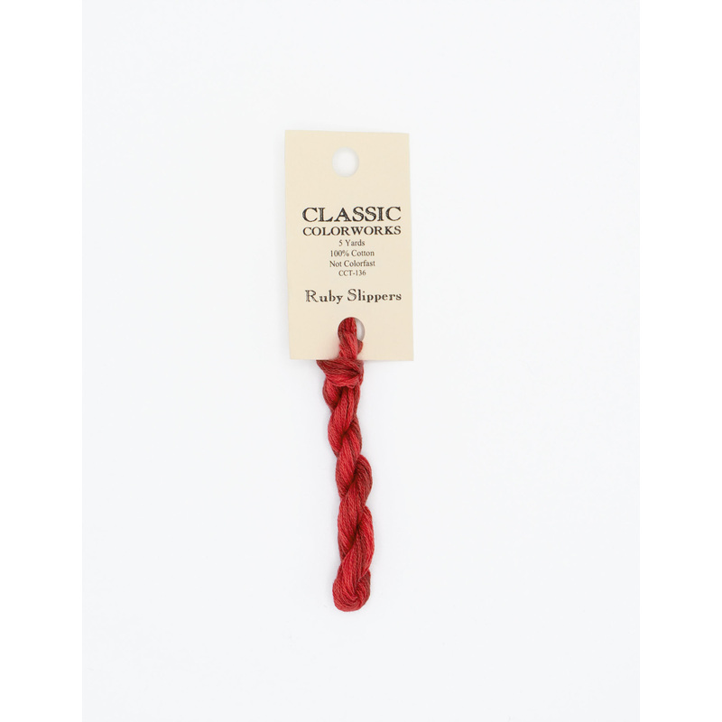 A skein of crimson red embroidery floss, twisted and bundled, with a cream and black label featuring the brand name and color information.