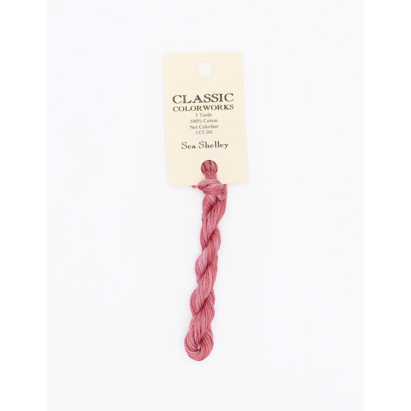 A skein of coral pink embroidery floss, twisted and bundled, with a cream and black label featuring the brand name and color information.