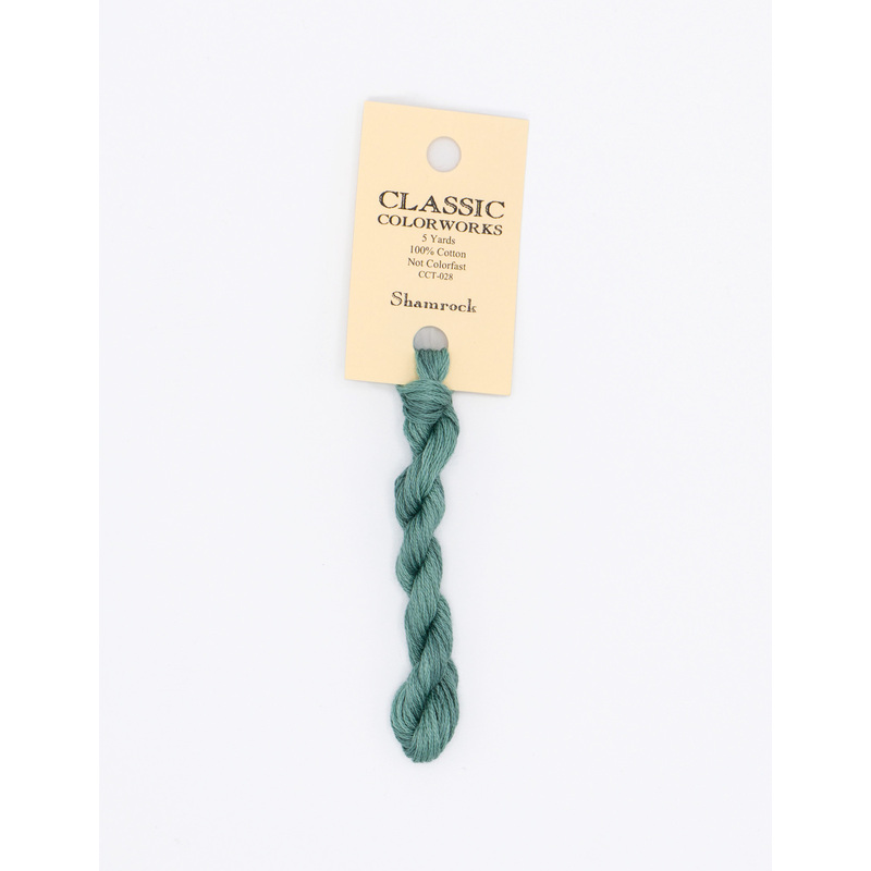A skein of teal embroidery floss, twisted and bundled, with a cream and black label featuring the brand name and color information.