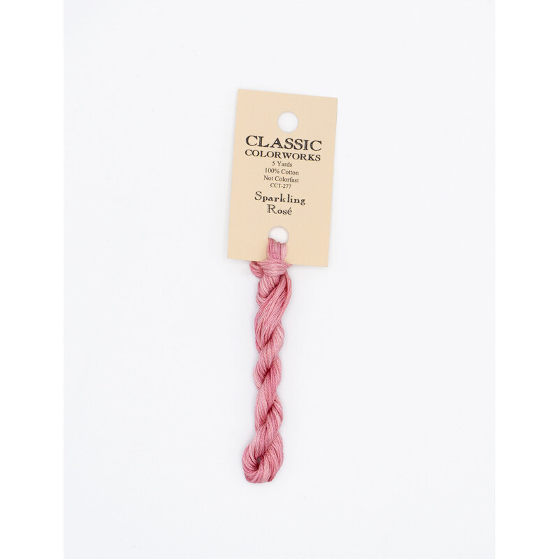 A skein of rose pink embroidery floss, twisted and bundled, with a cream and black label featuring the brand name and color information.