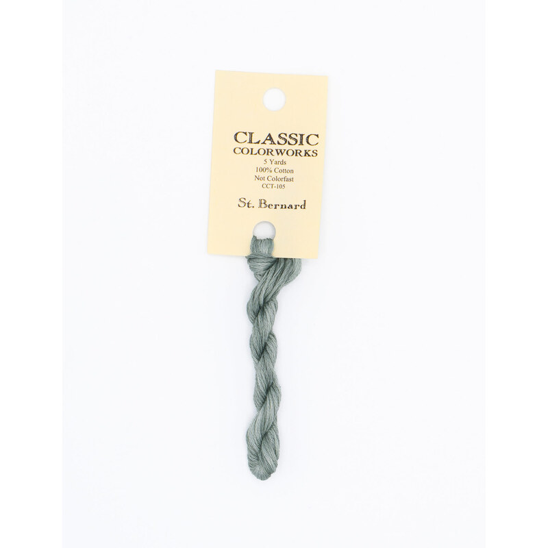 A skein of blue gray embroidery floss, twisted and bundled, with a cream and black label featuring the brand name and color information.
