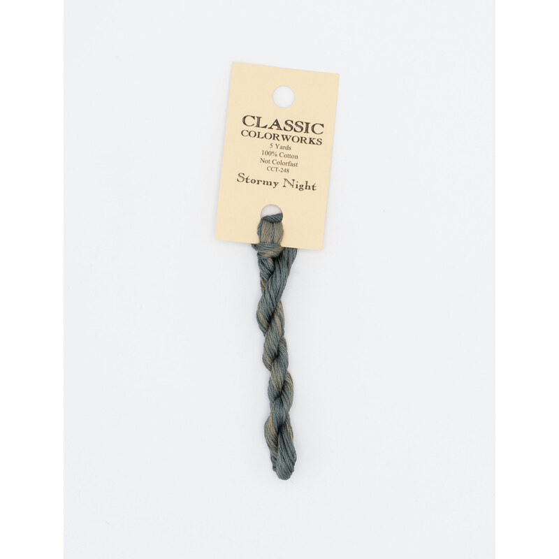 A skein of blue gray embroidery floss, twisted and bundled, with a cream and black label featuring the brand name and color information.