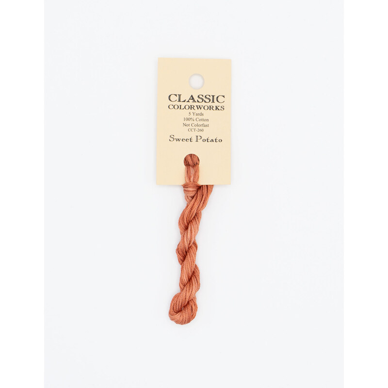 A skein of soft orange embroidery floss, twisted and bundled, with a cream and black label featuring the brand name and color information.