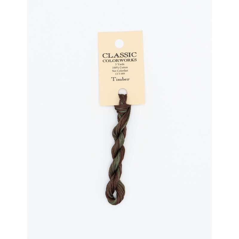 A skein of variegated brown and green embroidery floss, twisted and bundled, with a cream and black label featuring the brand name and color information.