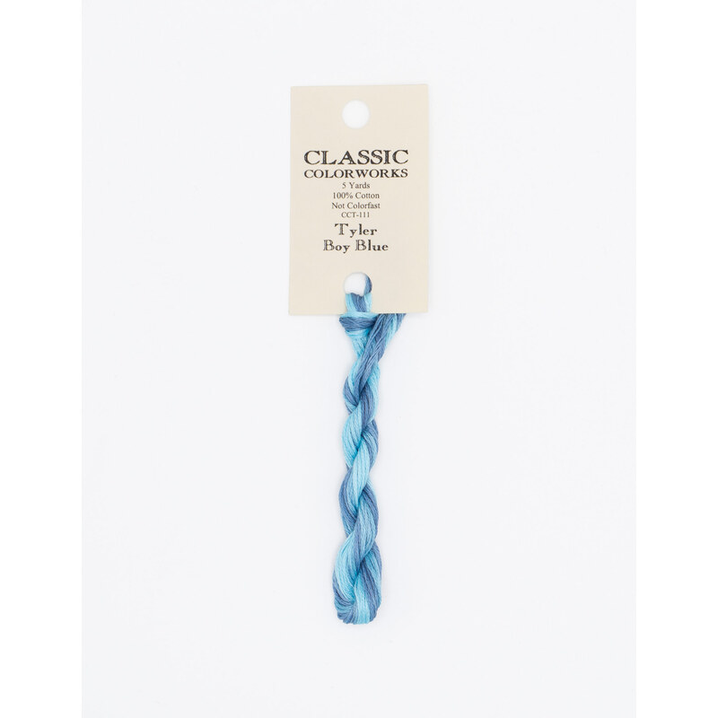 A skein of variegated blue and light blue embroidery floss, twisted and bundled, with a cream and black label featuring the brand name and color information.