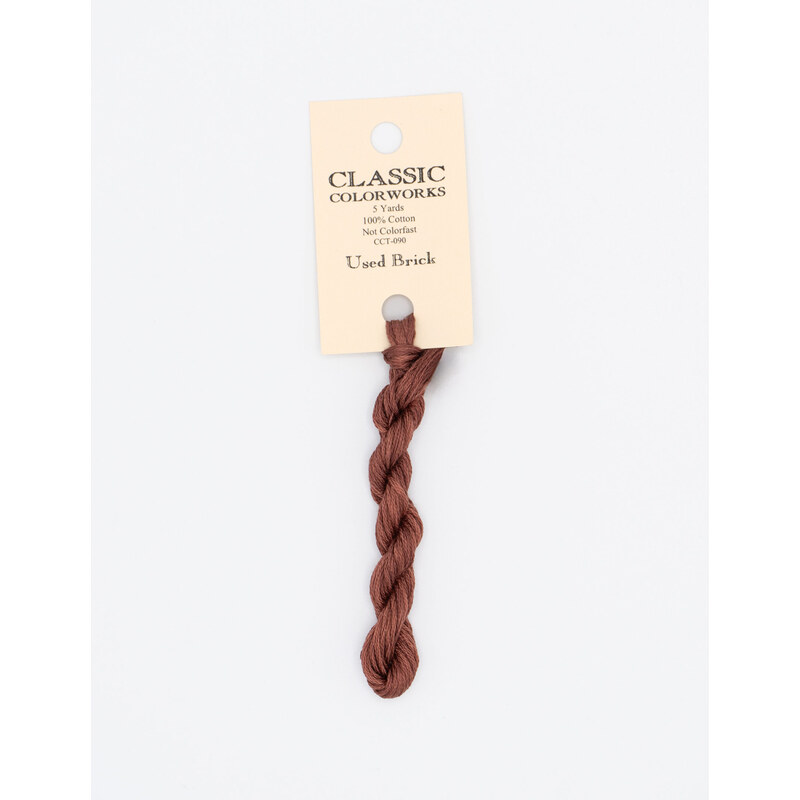 A skein of brick red embroidery floss, twisted and bundled, with a cream and black label featuring the brand name and color information.