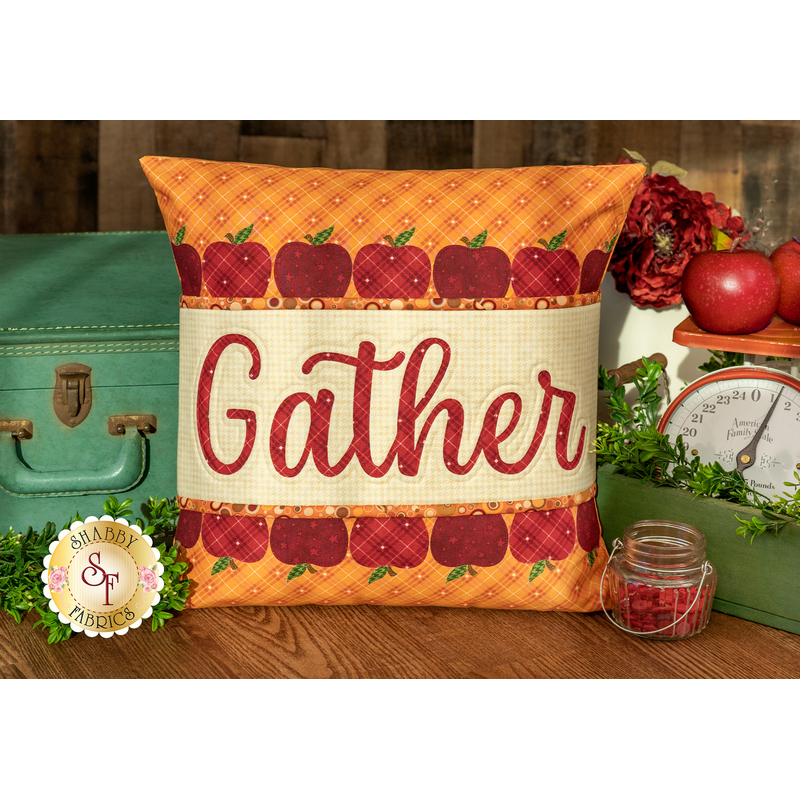The finished Gather pillow wrap kit, a red and orange wrap with red apple borders and appliqué letters that read 