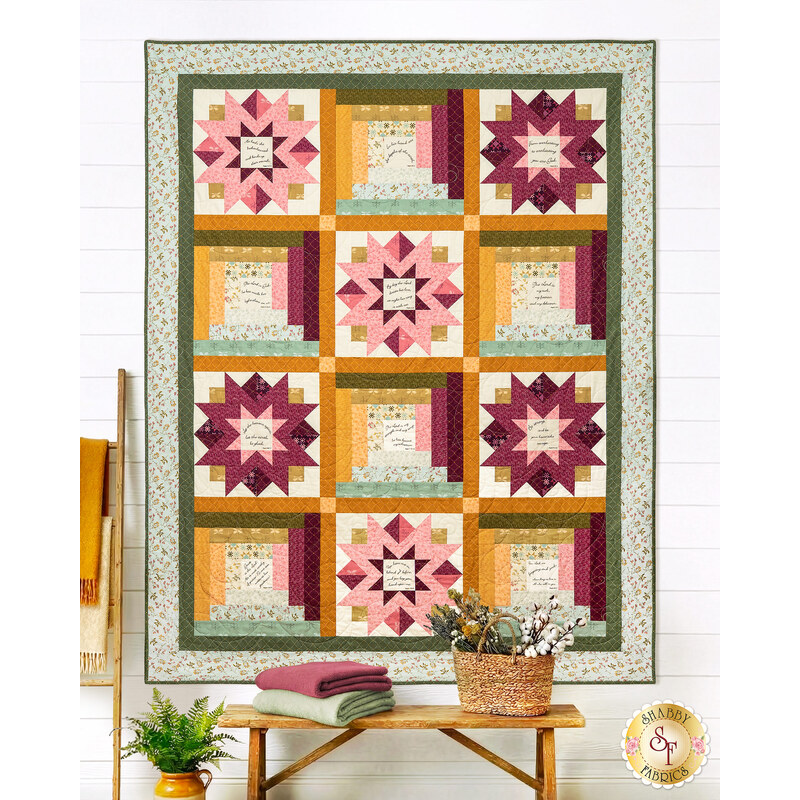 The completed Patchwork of Praise Quilt, colored in aqua, evergreen, gold, pink, and magenta fabrics from the Meadow Walk collection by Andover Fabrics, staged on a white wall with coordinating décor and furniture. 