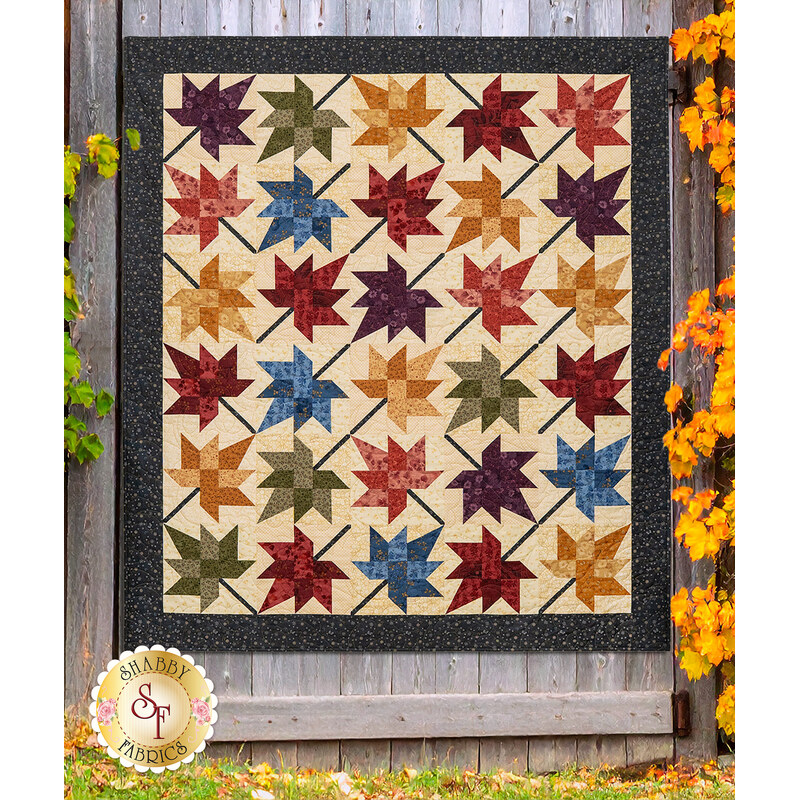 The Fluttering Leaves quilt, colored in colorful fabrics from the Flossie's Flowers collection by Henry Glass and hung on a gray wooden fence, framed by autumn trees.