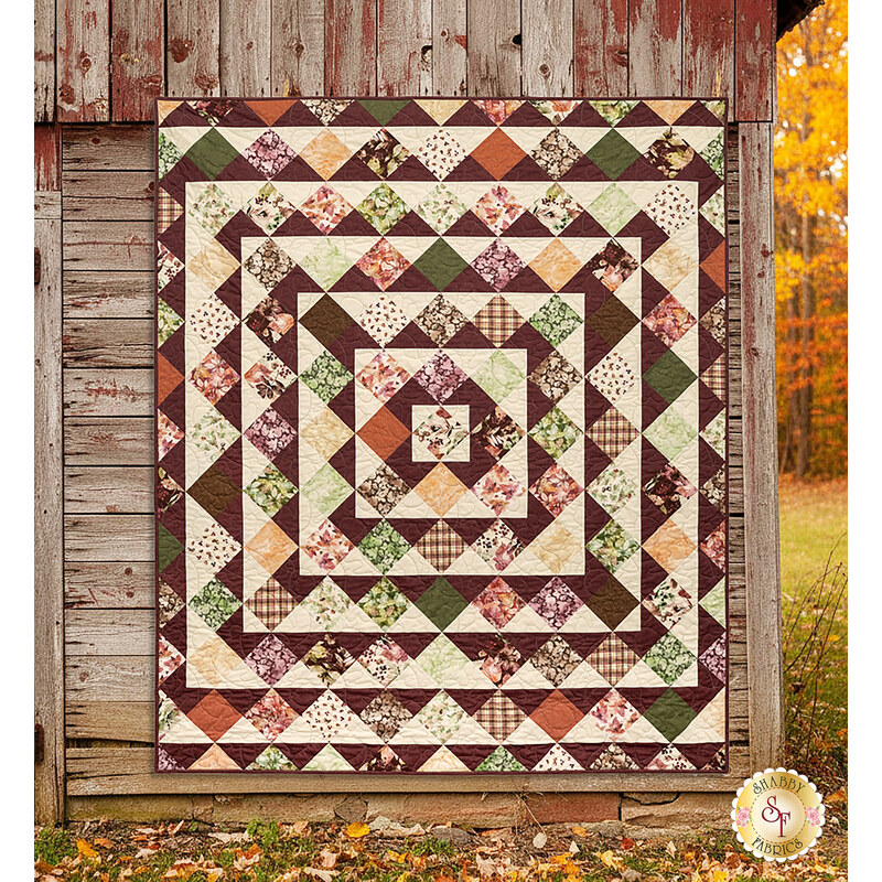 The completed Skip to My Lou Quilt colored in the warm prints of the Rustle collection, hung on a rustic wood-paneled barn in an autumn forest.