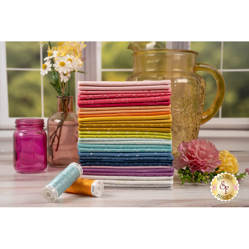 Stack of the fabrics included in the essence collection, with flowers, jars, thread and pitcher.
