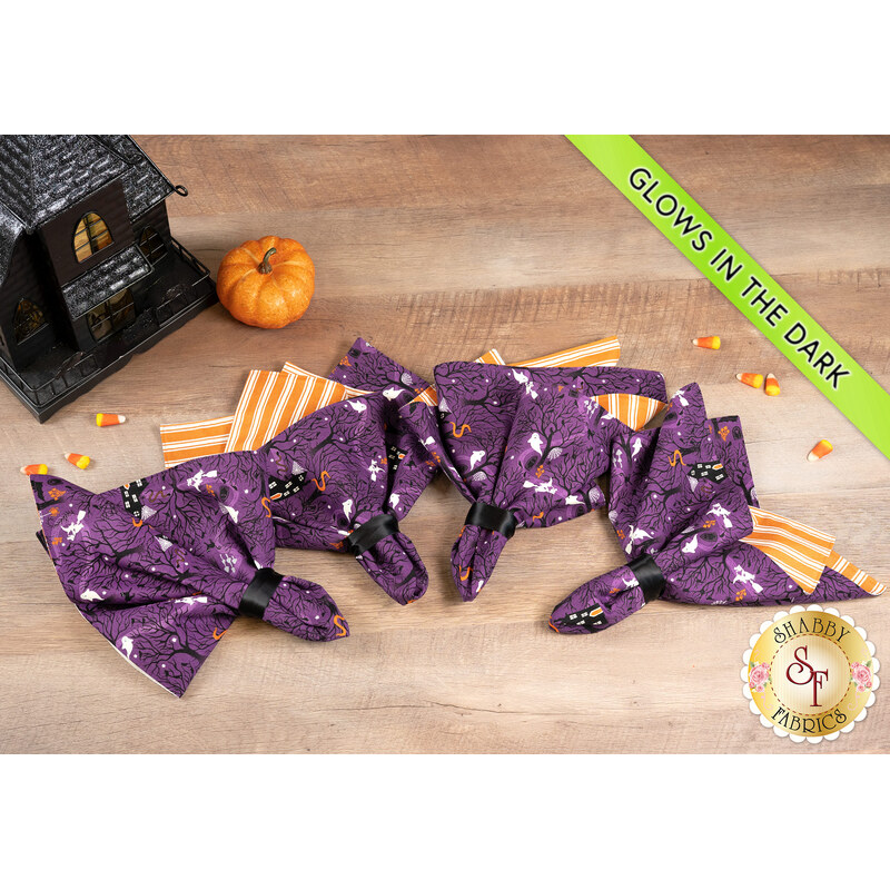 A top down shot of the completed napkins colored in purple and orange Halloween-themed fabrics from the Witchy Woods collection, staged on a wooden table with coordinating seasonal decor.