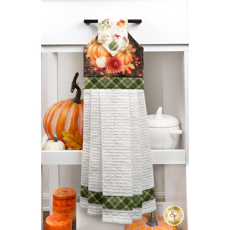 The completed Pumpkins themed hanging towel, colored in bright fall fabrics from the Gather With A Grateful Heart collection by Timeless Treasures Fabrics, staged on a kitchen drawer with coordinating decor.