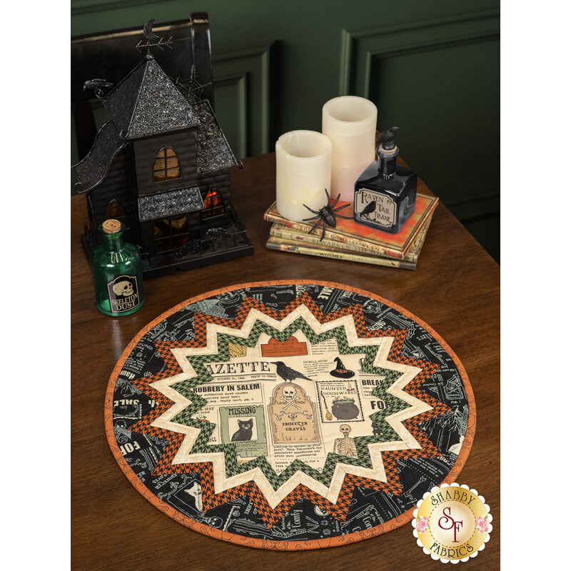 The completed Point of View Folded Star Table Topper colored in black, orange, green, and cream fabrics from the Home Sweet Haunt collection. The topper is staged on a wood table with coordinating Halloween decor and tableware.