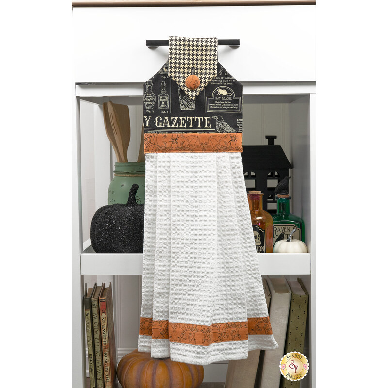 The completed black hanging towel, colored in Halloween fabrics from the Home Sweet Haunt collection, staged on a kitchen drawer with coordinating decor.