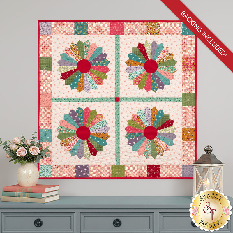 The completed Dresden Wall Hanging, colored in lovely pink, green, orange, teal, red, and purple calico fabrics from the Gentler Times collection. The project is hung on a gray wall and staged with coordinating gentle décor.