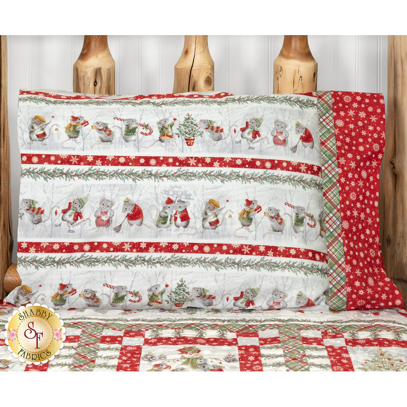 The completed Magic Pillowcase colored in gray, white, red, and green flannel fabrics from The Christmas Mouse collection by Northcott Fabrics, staged on a wood log bed with the coordinating Merry Mouse-mas quilt.