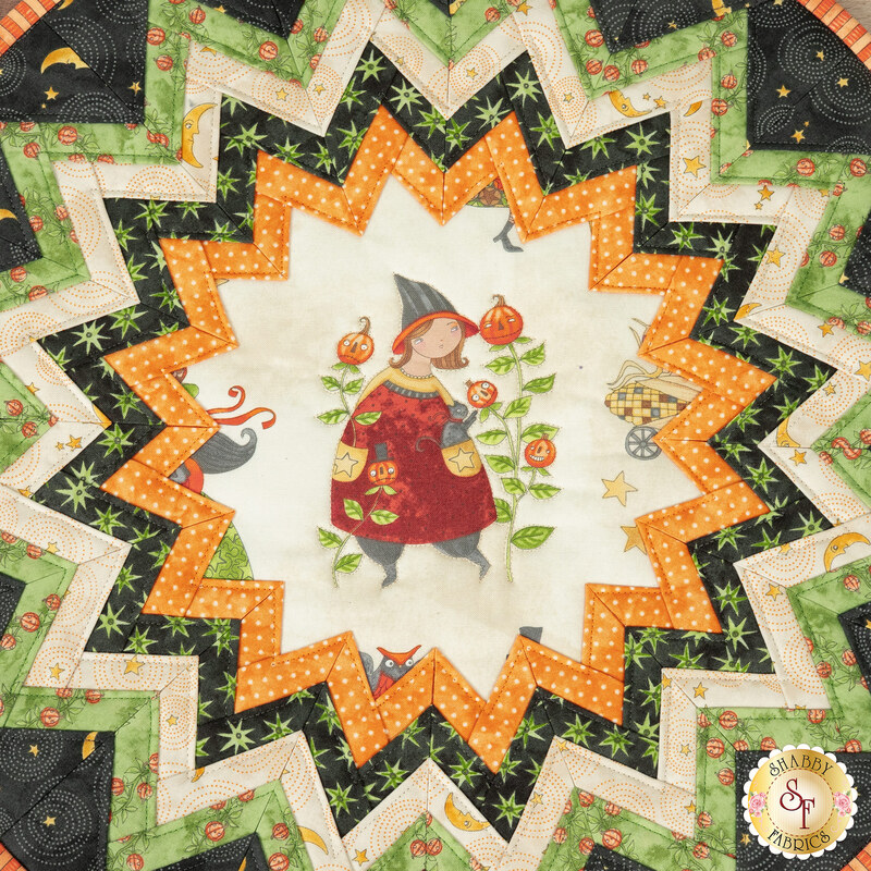 A super close up top-down shot of the folded star center, showcasing the cream fabric with a witch standing in her garden with stalks of enchanted pumpkins.