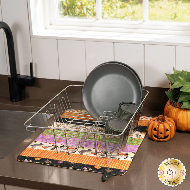 The completed Dry Ideas project, colored in Halloween fabrics from the Ghoul Friends collection, staged on a kitchen counter beside the sink and underneath a wire dish rack holding clean dishware.