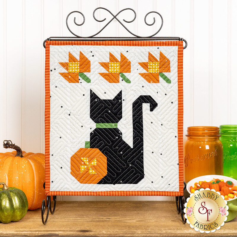 Halloween themed table top banner with orange leaves, a pumpkin, and a black cat on a white background, hung on a display hanger and staged with coordinating decor.