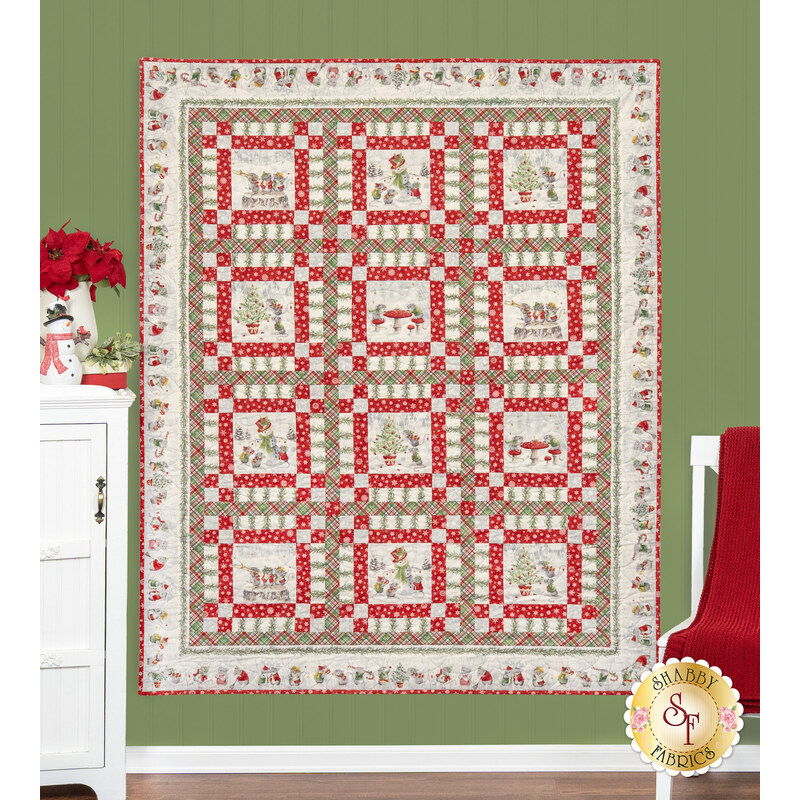 The completed Merry Mouse-mas Quilt, colored in gray, white, red, and green flannel fabrics from The Christmas Mouse collection by Northcott Fabrics, hung on a green paneled wall and staged with a coordinating pillow project, furniture, and decor.