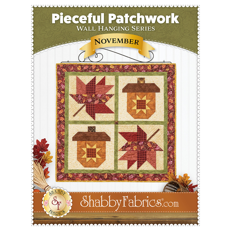 Front cover of the pattern showing the completed Pieceful Patchwork - November wall hanging, a square project with two patchwork acorns and leaves in autumn themed fabrics, staged on a white wall with coordinating decor.