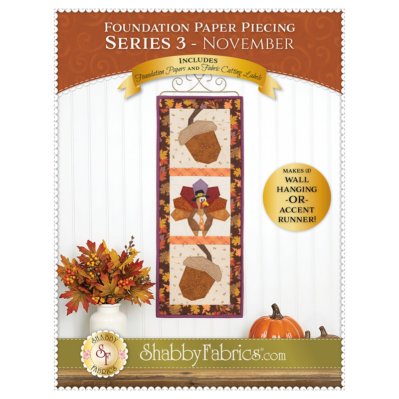 Front cover of the Foundation Paper Piecing Series 3 - November Pattern showing the completed wall hanging, hung on a white wall and staged with coordinating fall decor.