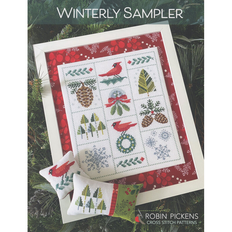A framed winter-themed cross-stitch sampler with red accents, featuring cardinals, pinecones, and snowflakes.