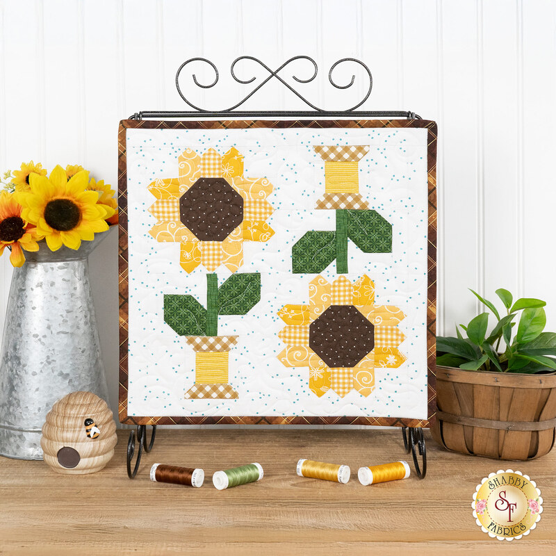 The completed August spool, two yellow, brown, and green spools, hung on a craft holder and staged on a wooden table with coordinating spools and decor.