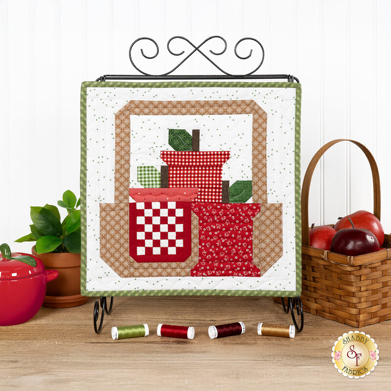 The completed September spool, three red apple themed spools, hung on a craft holder and staged on a wooden table with coordinating spools and decor.