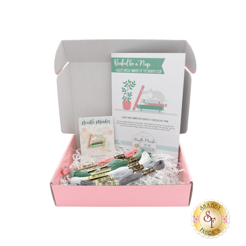 The August Needle Minder of the Month, a green, pink, and white project centered around a needle minder with a cat sleeping atop a stack of books.