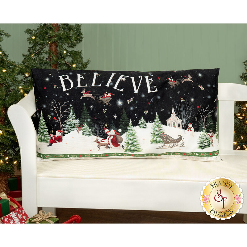 The completed Believe Pillow colored in the festive fabrics from the Believe collection, staged on a neutral couch in front of a decorated Christmas fireplace with stockings and garland.