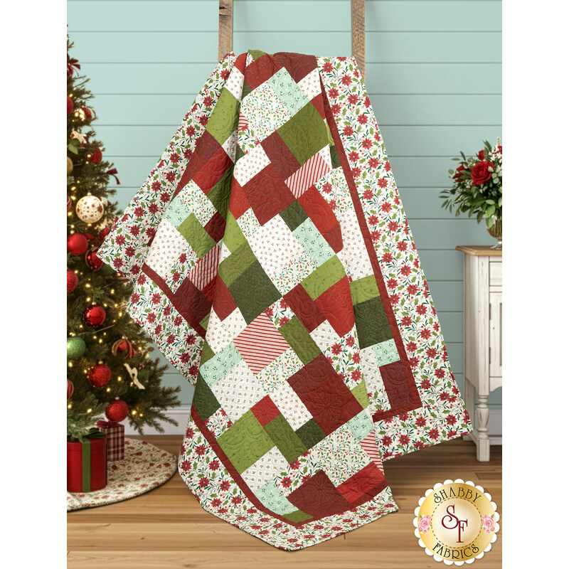 The completed Easy as ABC quilt in red, green, aqua, and cream fabrics from the Make it Merry collection by Marcus Fabrics, artfully draped over a wooden ladder and staged with coordinating flowers and holiday furniture.