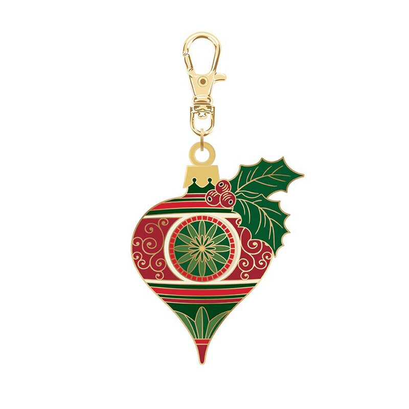 Gold keychain charm shaped like a Christmas ornament with red and green sophisticated designs and holly..