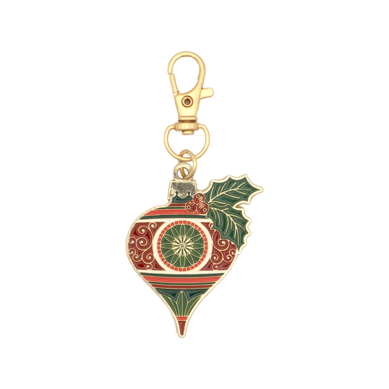 Gold keychain charm shaped like a Christmas ornament with red and green sophisticated designs and holly..