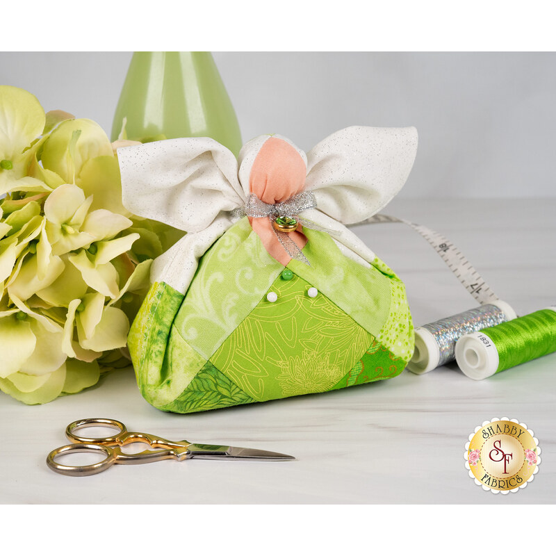 The completed August Birthstone Angel with a bright chartreuse palette, white wings, a silver bow and bright green charm beside coordinating decor and notions.