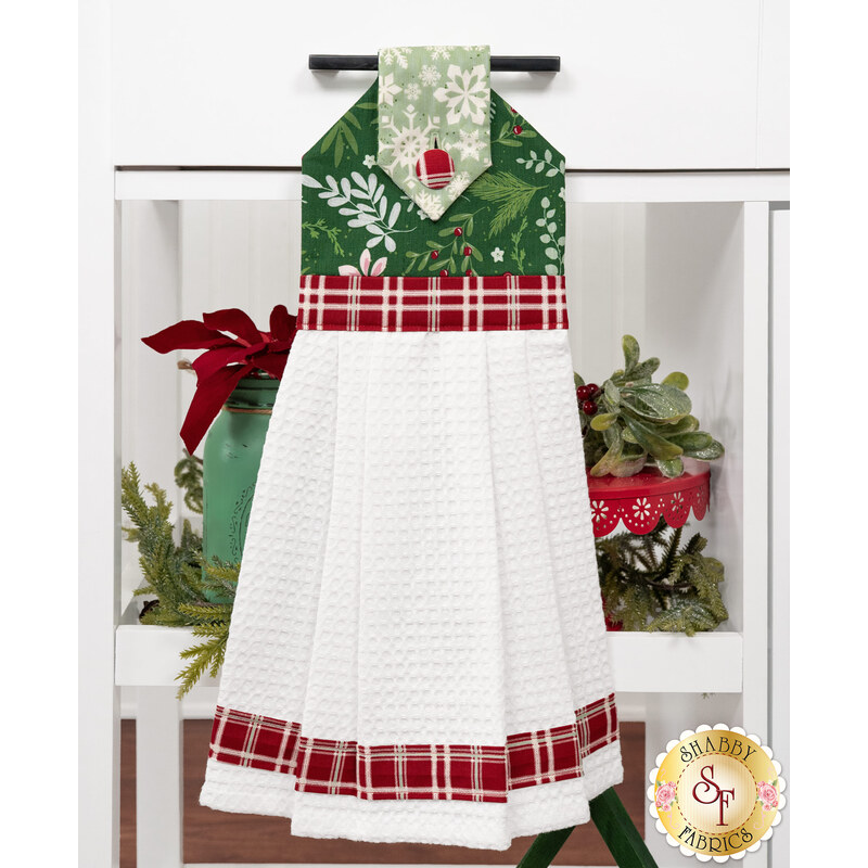 The completed hanging towel staged on a kitchen drawer, colored in green, mint, and red fabrics from the Mistletoe & Holly collection. Coordinating festive decor peeks in from behind the towel.